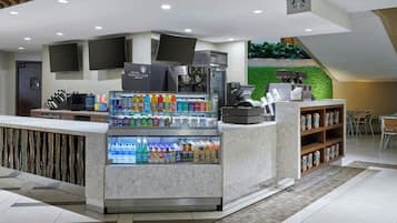 Una cafetería moderna con mostrador de mármol, exhibidor refrigerado de bebidas y una pared verde.
