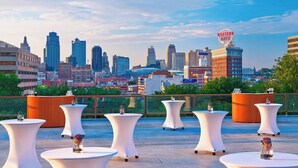A rooftop terrace with white tables and chairs, a city skyline in the background, and a Western Auto sign. - The Westin Kansas City at Crown Center (Kansas City)