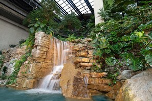 Ein Wasserfall stürzt über einen Felsvorsprung, umgeben von üppiger Vegetation in einer Innenraumgestaltung.