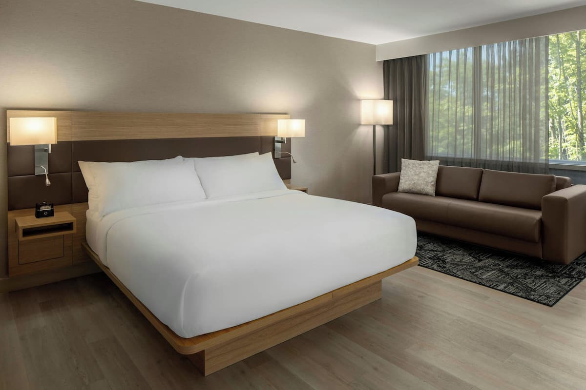 A modern hotel room with a large bed, a sofa, and a nightstand with a lamp.