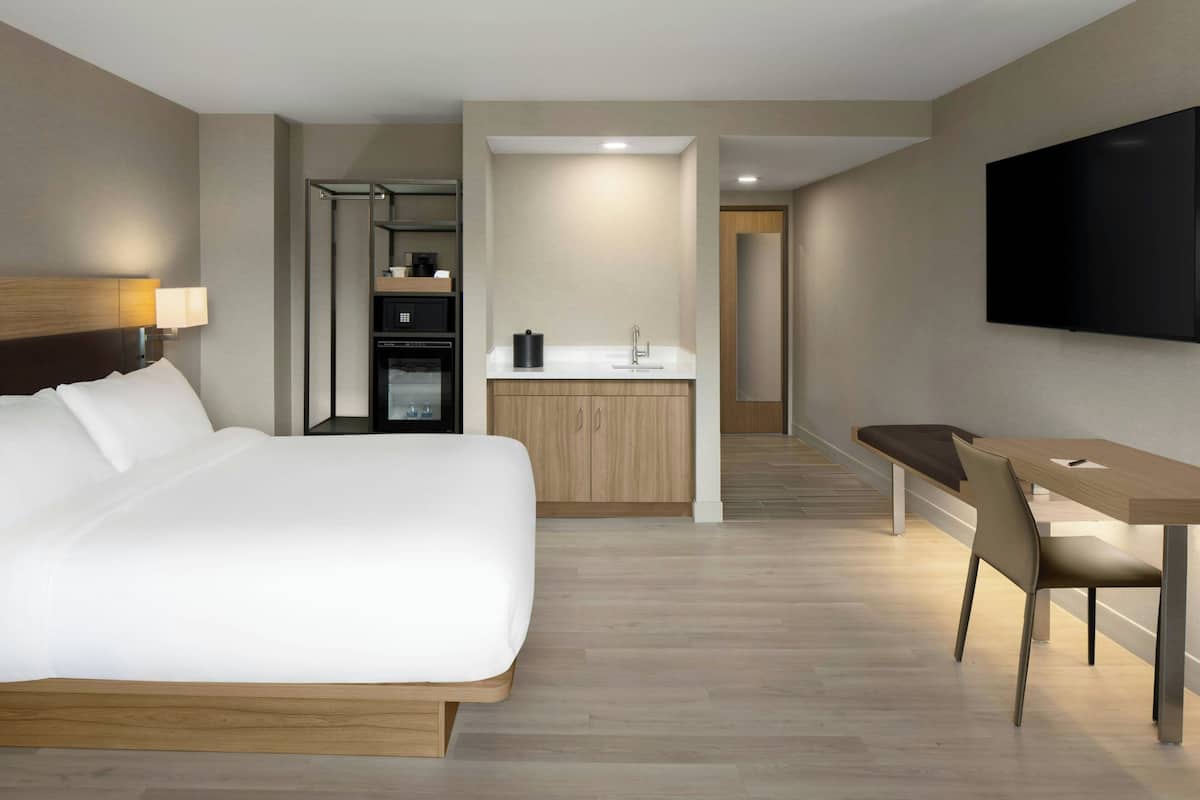 A hotel room with a large bed, a desk, a flat-screen TV, and a kitchenette.