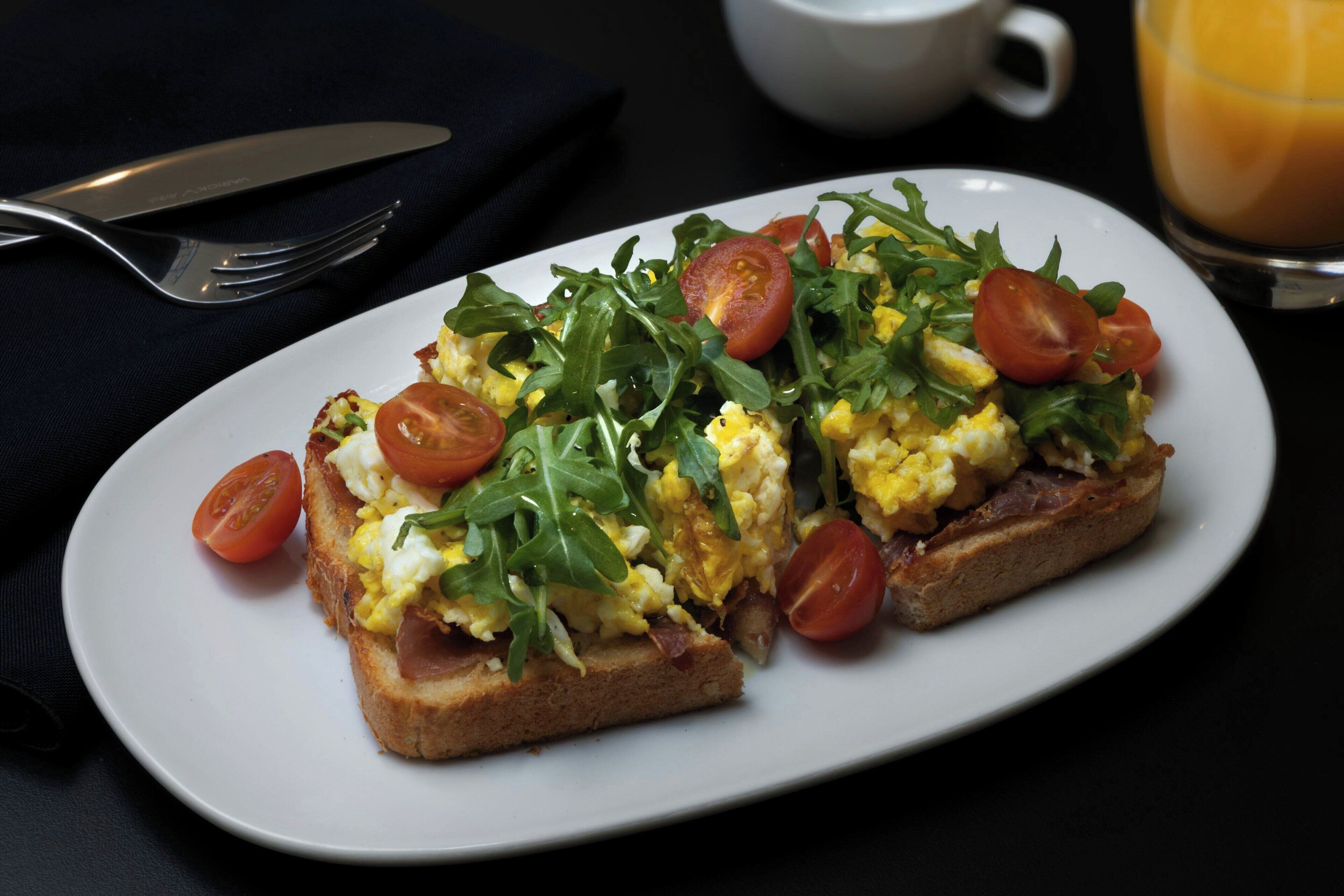 A breakfast plate with toast, scrambled eggs, arugula, and cherry tomatoes.