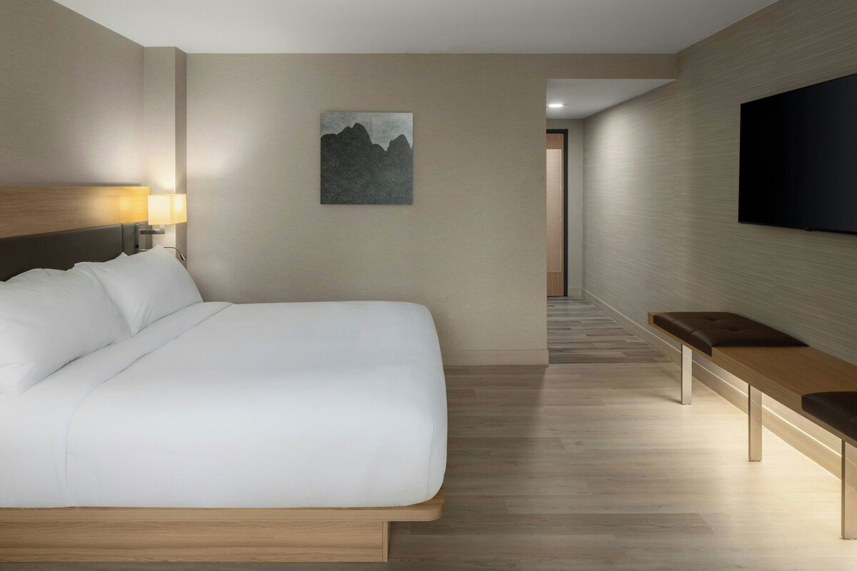 A modern hotel room with a large bed, a bedside table, a flat-screen TV, and a painting on the wall.