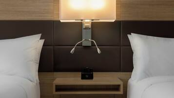 A hotel room with a bed, bedside tables, a nightstand, and a wall-mounted lamp.