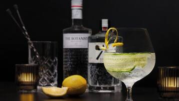 Un verre à cocktail orné d’une tranche de concombre et d’une rondelle de citron, une bouteille de spiritueux, un verre et une moitié de citron, le tout posé sur une surface sombre.