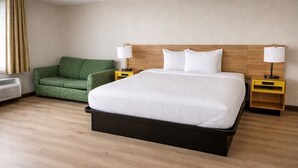 A hotel room with a bed, a green sofa, two bedside tables with lamps, and a wall-mounted heater.