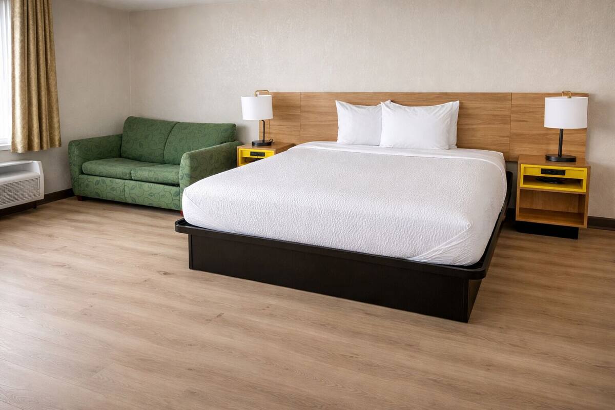 Ein Hotelzimmer mit einem Bett, einem grünen Sofa, zwei Nachttischen mit Lampen und einer Wandheizung.