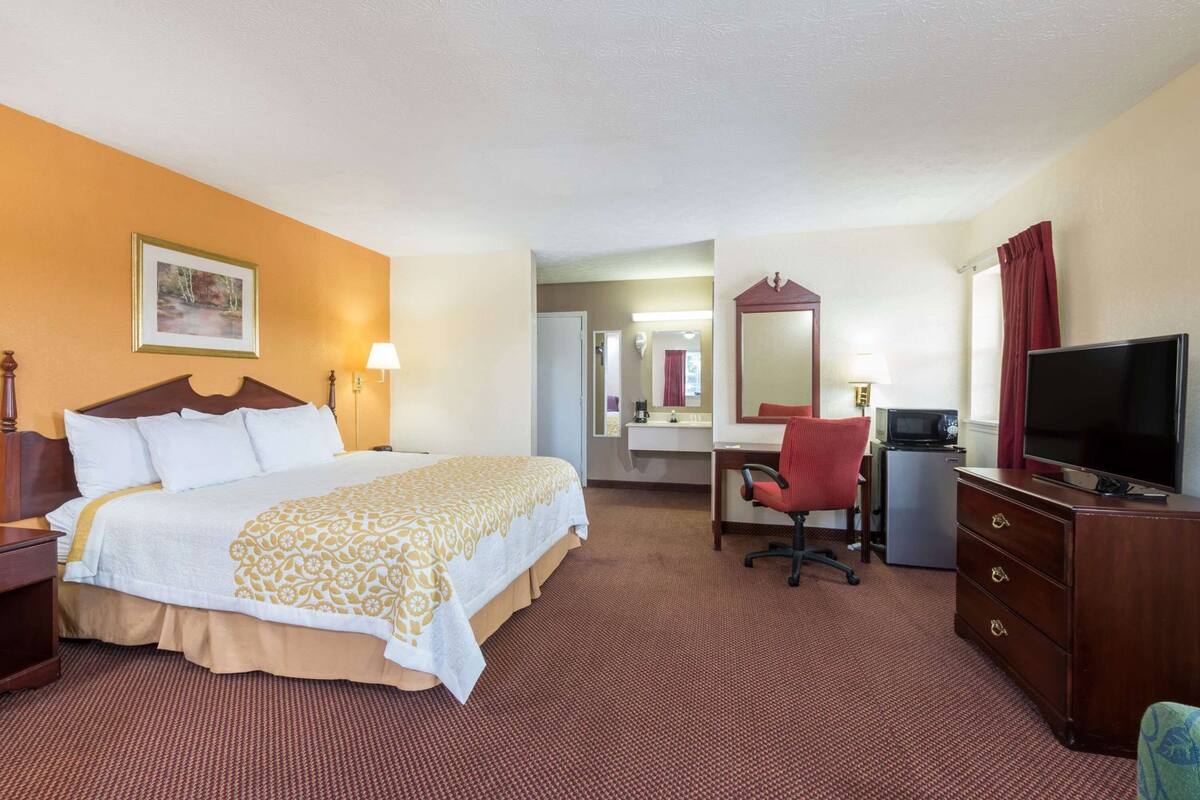 Ein Hotelzimmer mit Bett, Schreibtisch, Stuhl, Fernseher und Spiegel.