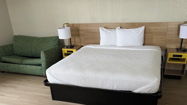 A hotel room with a bed, two bedside tables, a green sofa, and a wooden floor.