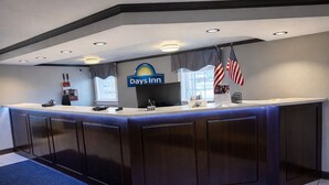 A reception desk at Days Inn with a blue carpet, a sign, and two American flags.