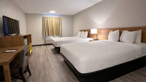 Une chambre d’hôtel avec deux lits, un bureau avec une télévision, une fenêtre avec des rideaux et un luminaire au plafond.