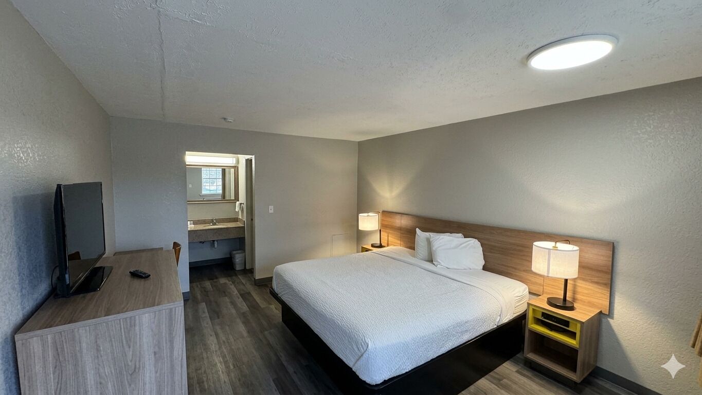 Una habitación de hotel con una cama, lámparas de noche, un escritorio con una computadora y un televisor.