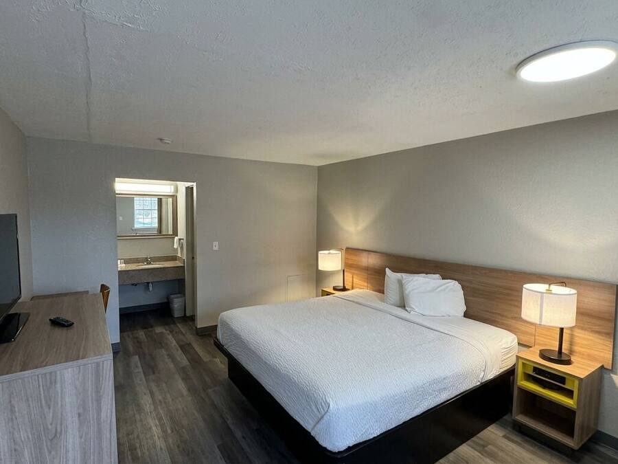 A hotel room with a bed, bedside lamps, a desk with a computer, and a television.