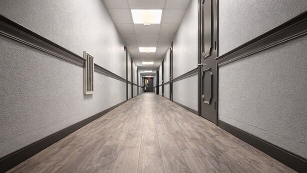 Un long couloir étroit doté d’un plancher en bois et de murs de couleur gris clair.