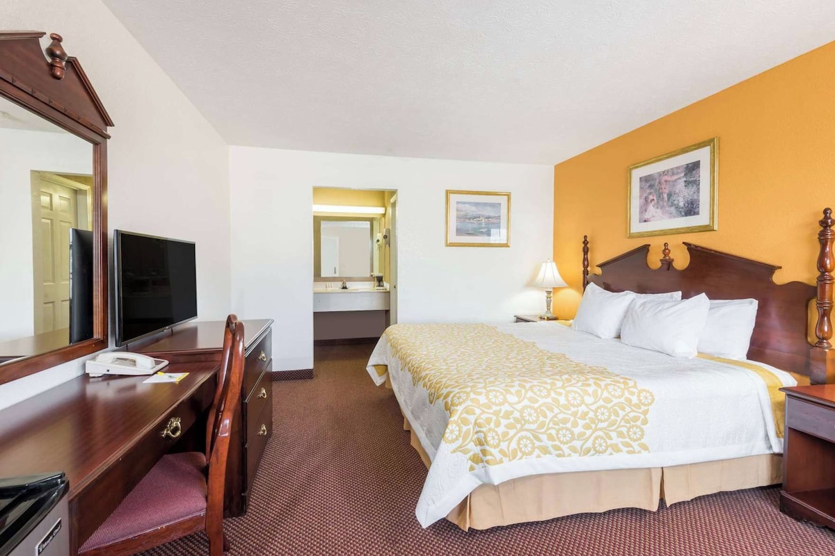 A hotel room with a bed, a desk with a telephone, a television, a mirror, and a bathroom visible through an open door.