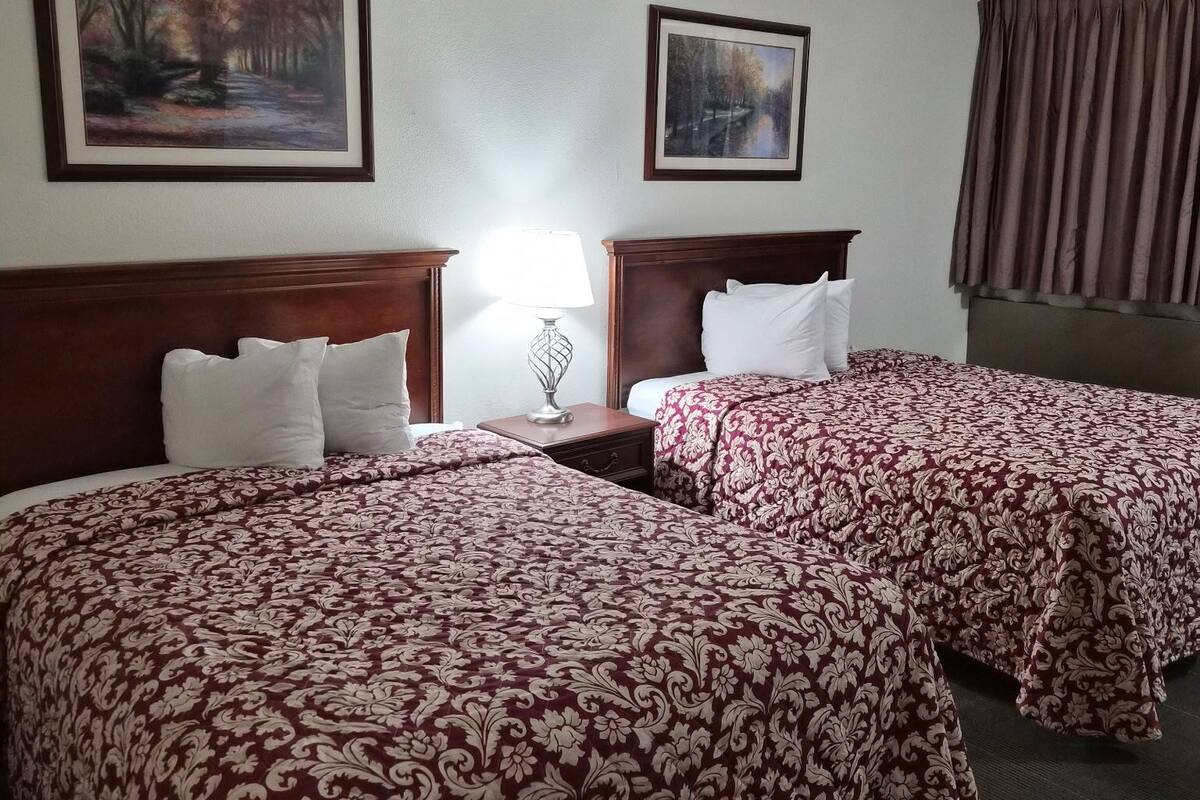 A hotel room with two beds, each with a floral-patterned bedspread, a nightstand with a lamp, and two framed pictures on the wall.