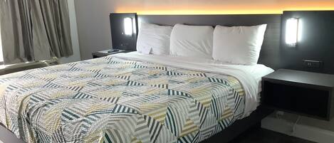 Una habitación de hotel moderna con una cama grande, cabecero con iluminación integrada, mesita de noche y ventana con cortinas.