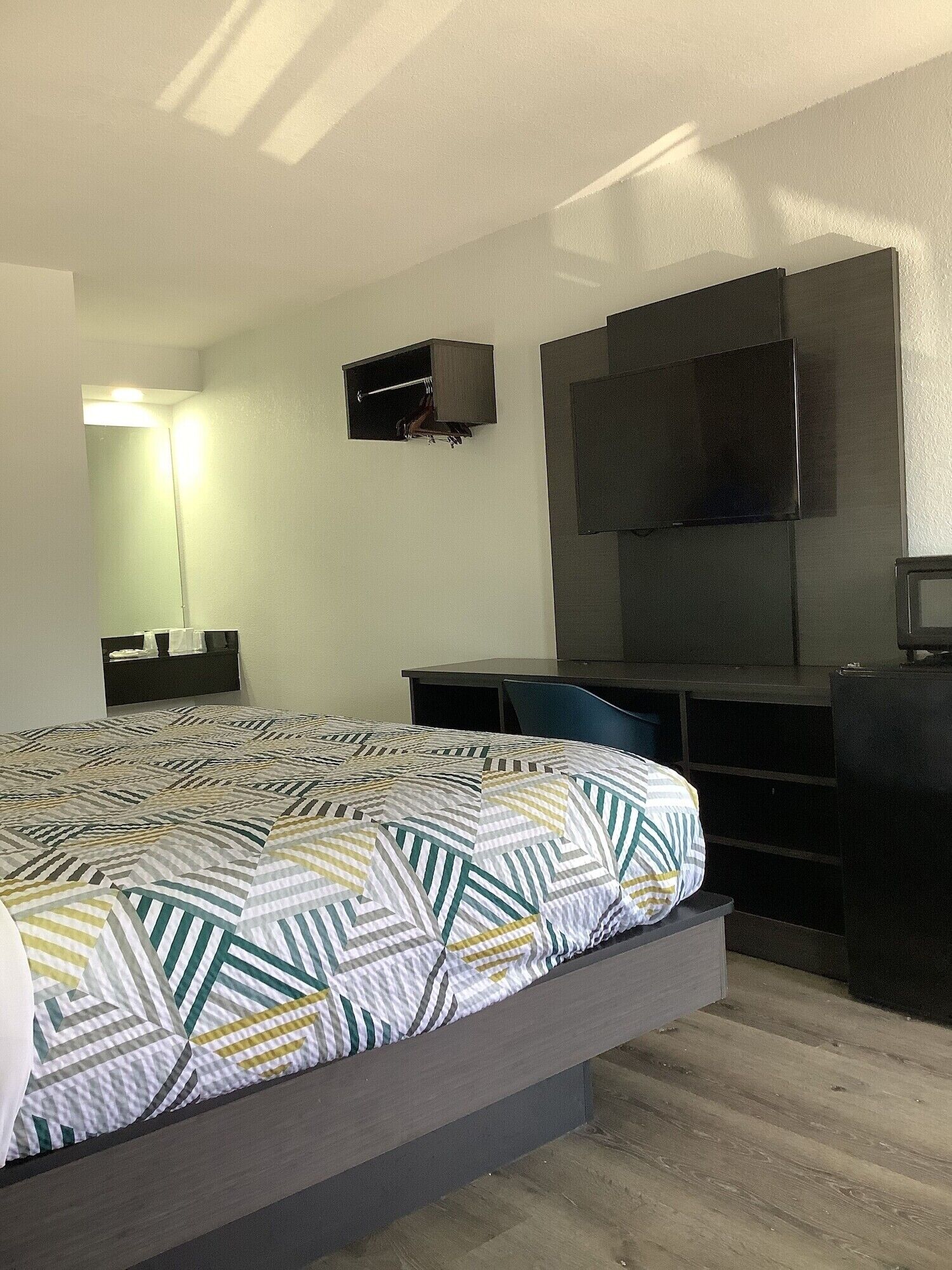 Una habitación de hotel moderna con una cama, un escritorio, una silla, un televisor montado en la pared y un espejo.