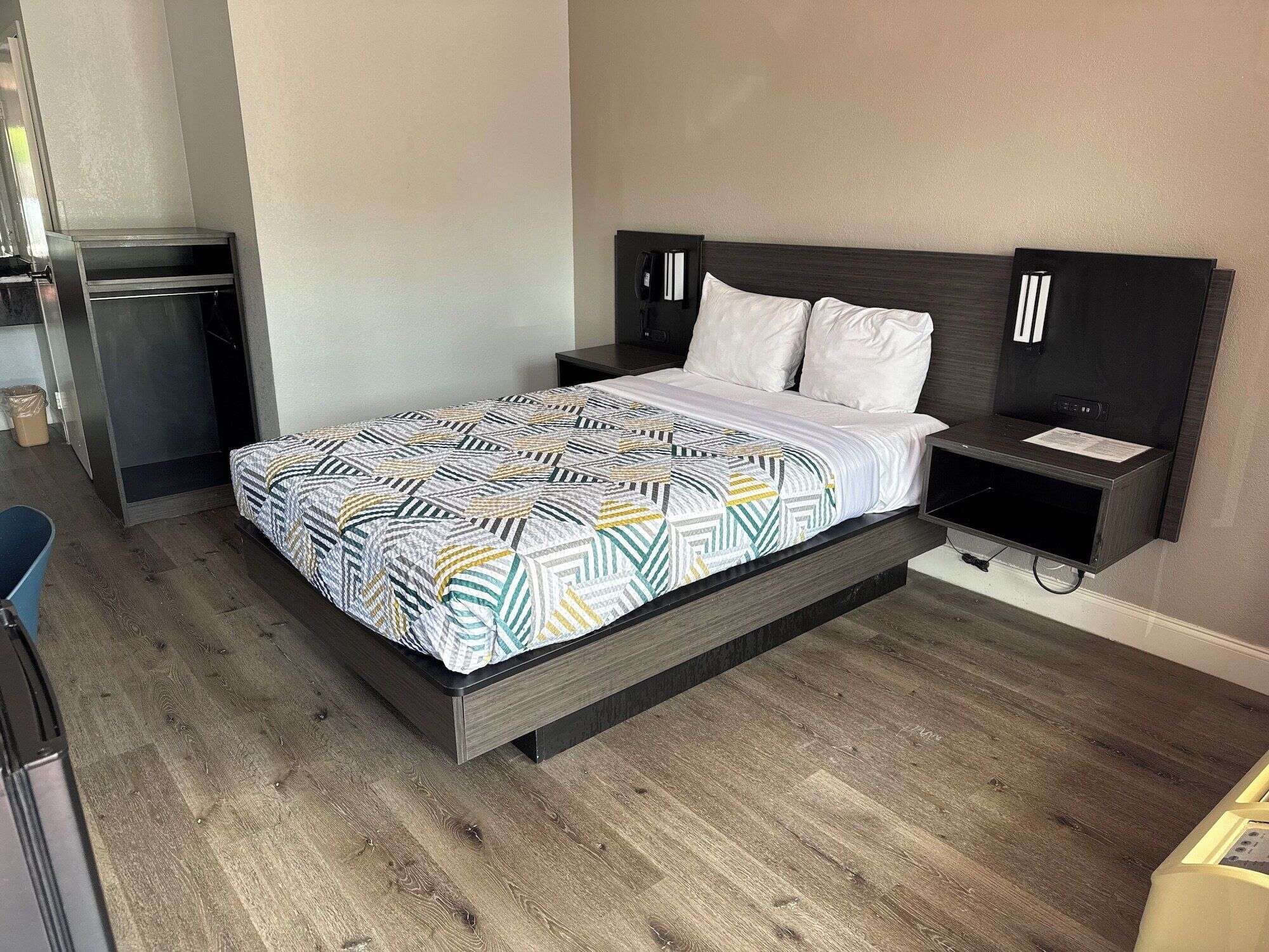 A modern hotel room with a bed, bedside tables, a desk, and a wardrobe.