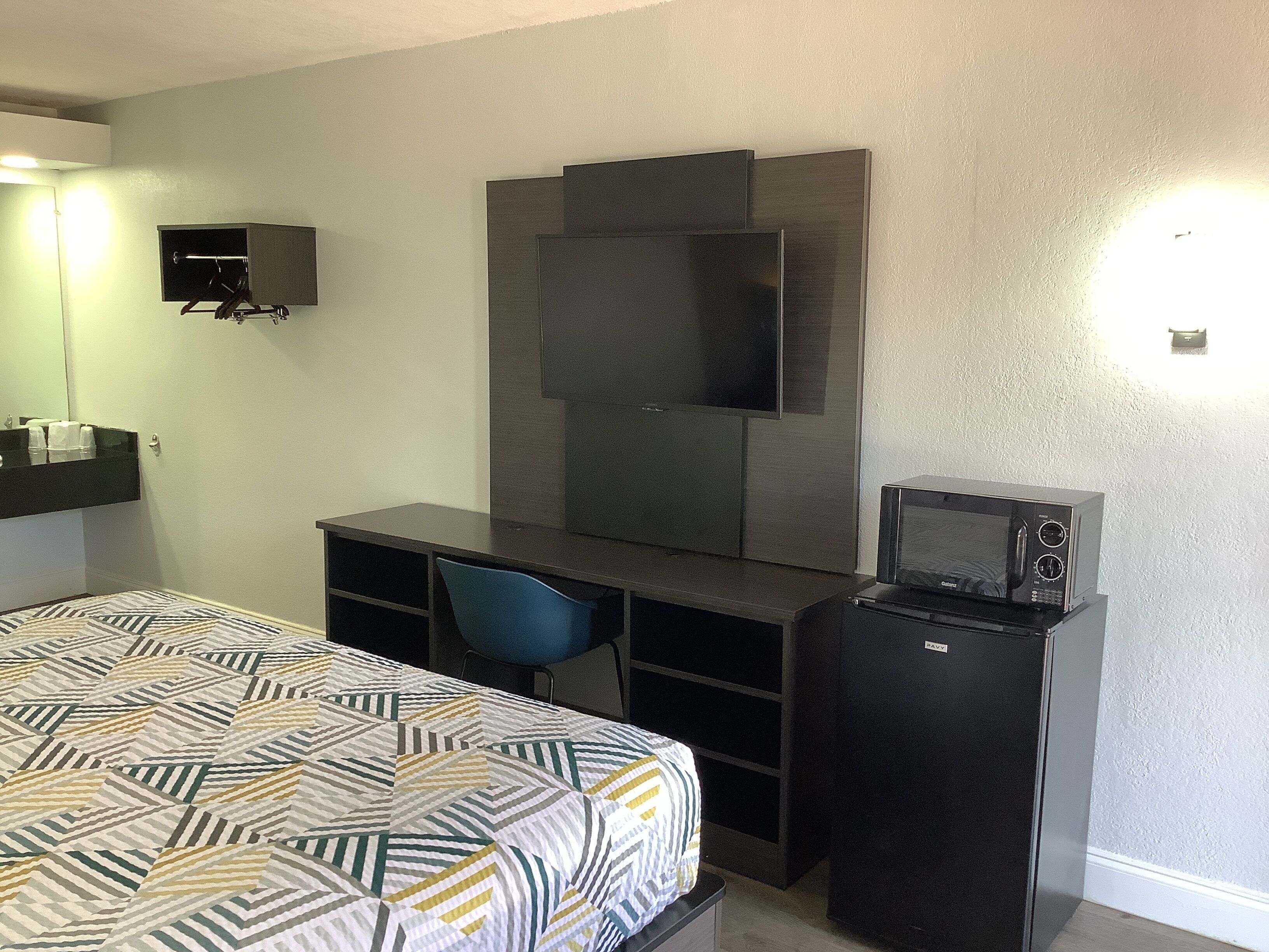 A hotel room with a bed, a desk with a chair, a television, and a microwave.