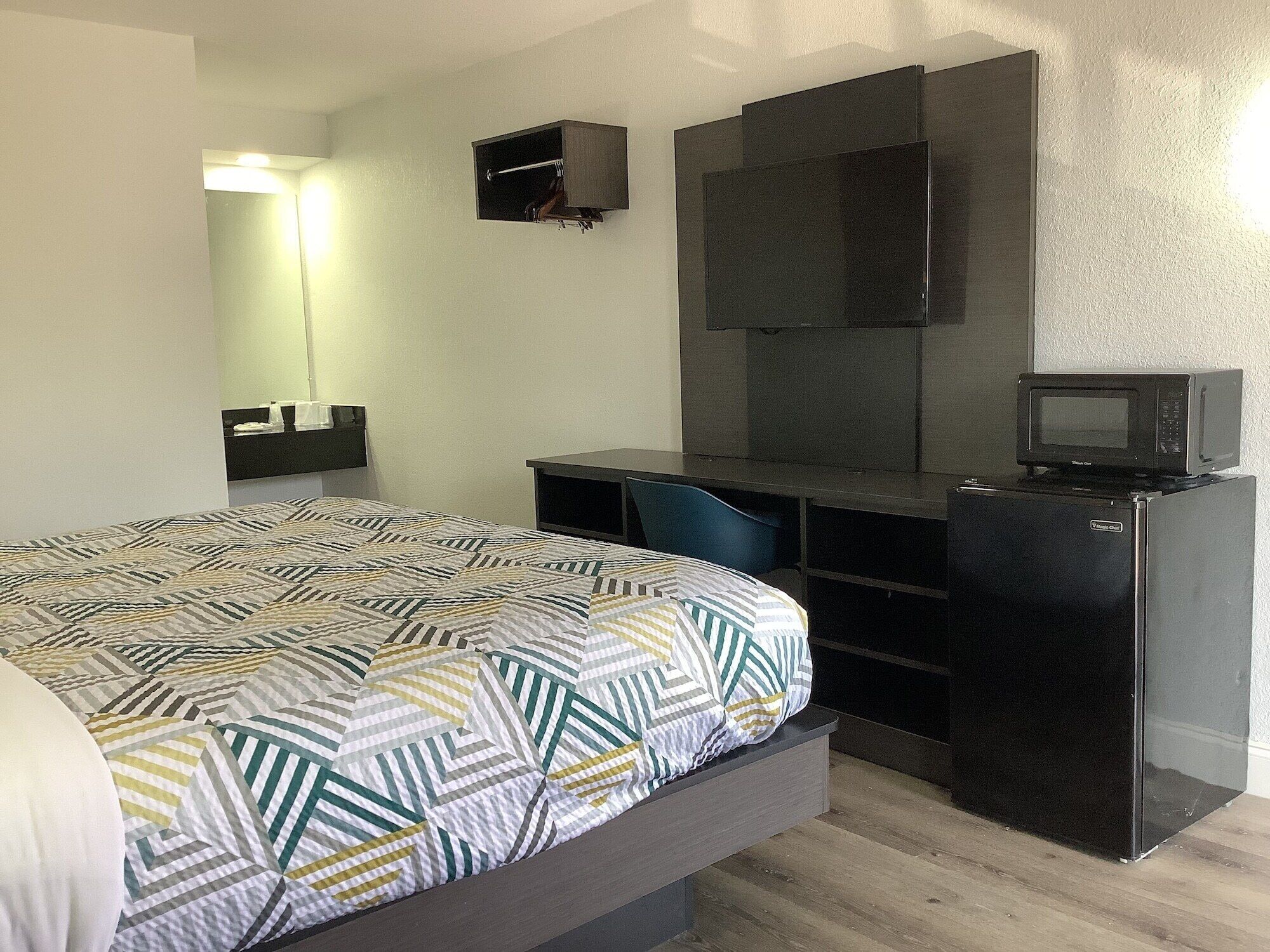 A hotel room with a bed, a desk, a chair, a TV, and a microwave.