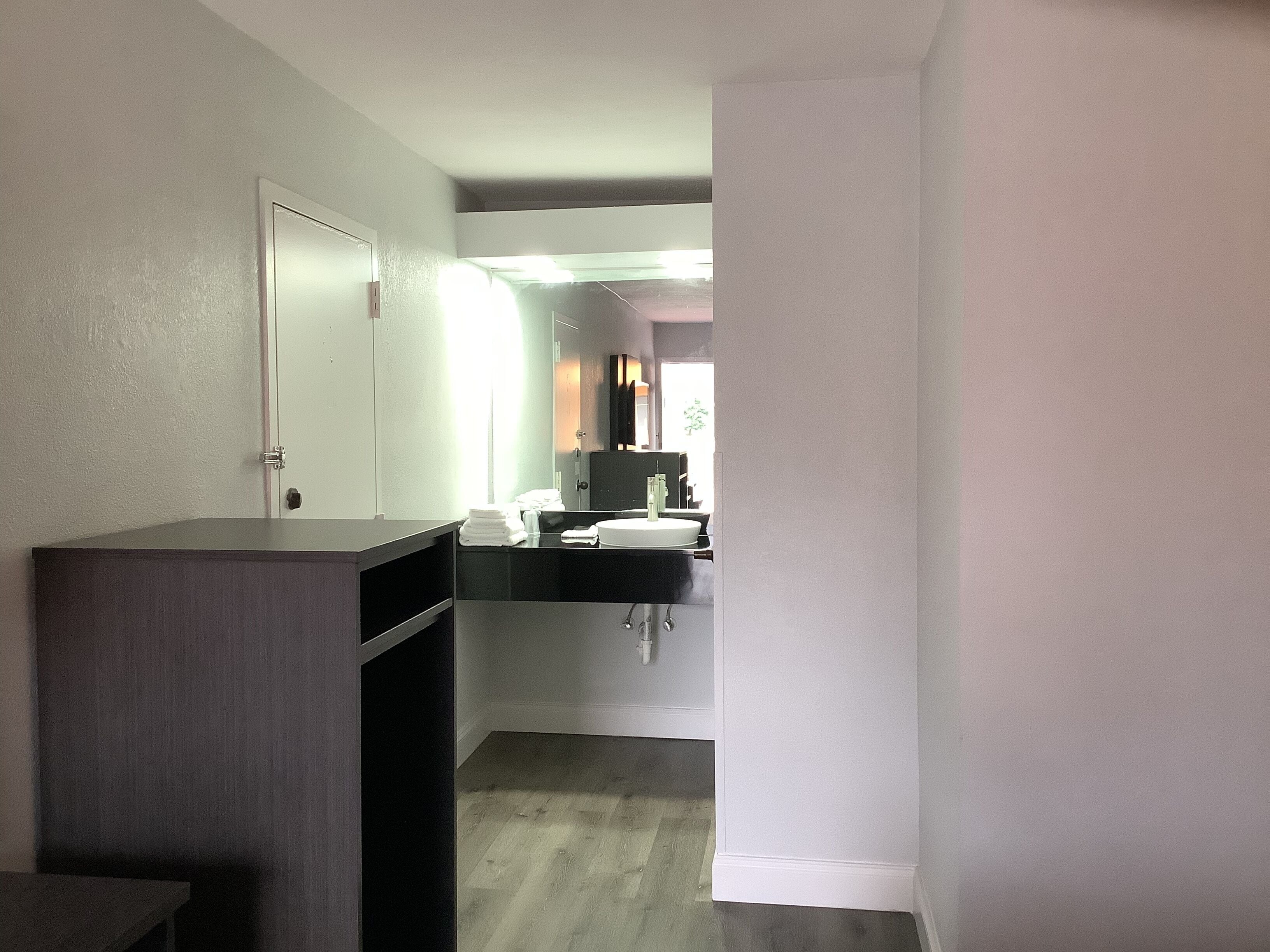 A hotel room with a dark wooden desk, a white sink, and a mirror.