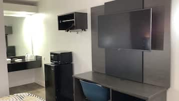 Une chambre d’hôtel équipée d’un lit, d’un bureau avec une chaise, d’une télévision, d’un four à micro-ondes et d’un petit réfrigérateur.