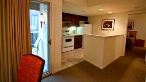 A compact kitchen with a refrigerator, microwave, and oven. There is a dining area with a chair and a table. The room has a sliding glass door leading to an outdoor area. - The Inn at Tallgrass (Wichita)
