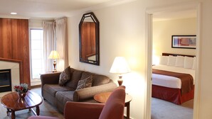 A hotel room with a sofa, armchair, and a bed with white bedding. - The Inn at Tallgrass (Wichita)