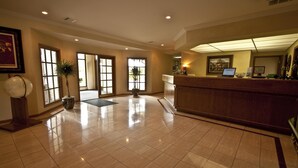A spacious lobby with a reception desk, large windows, and a potted plant. - The Inn at Tallgrass (Wichita)