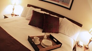 A neatly made bed with a tray of breakfast items, a framed picture on the wall, and a bedside table with a lamp. - The Inn at Tallgrass (Wichita)