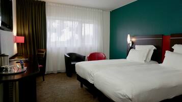 Una camera d'albergo con un letto grande, una scrivania con una lampada, una sedia e una finestra con tende.