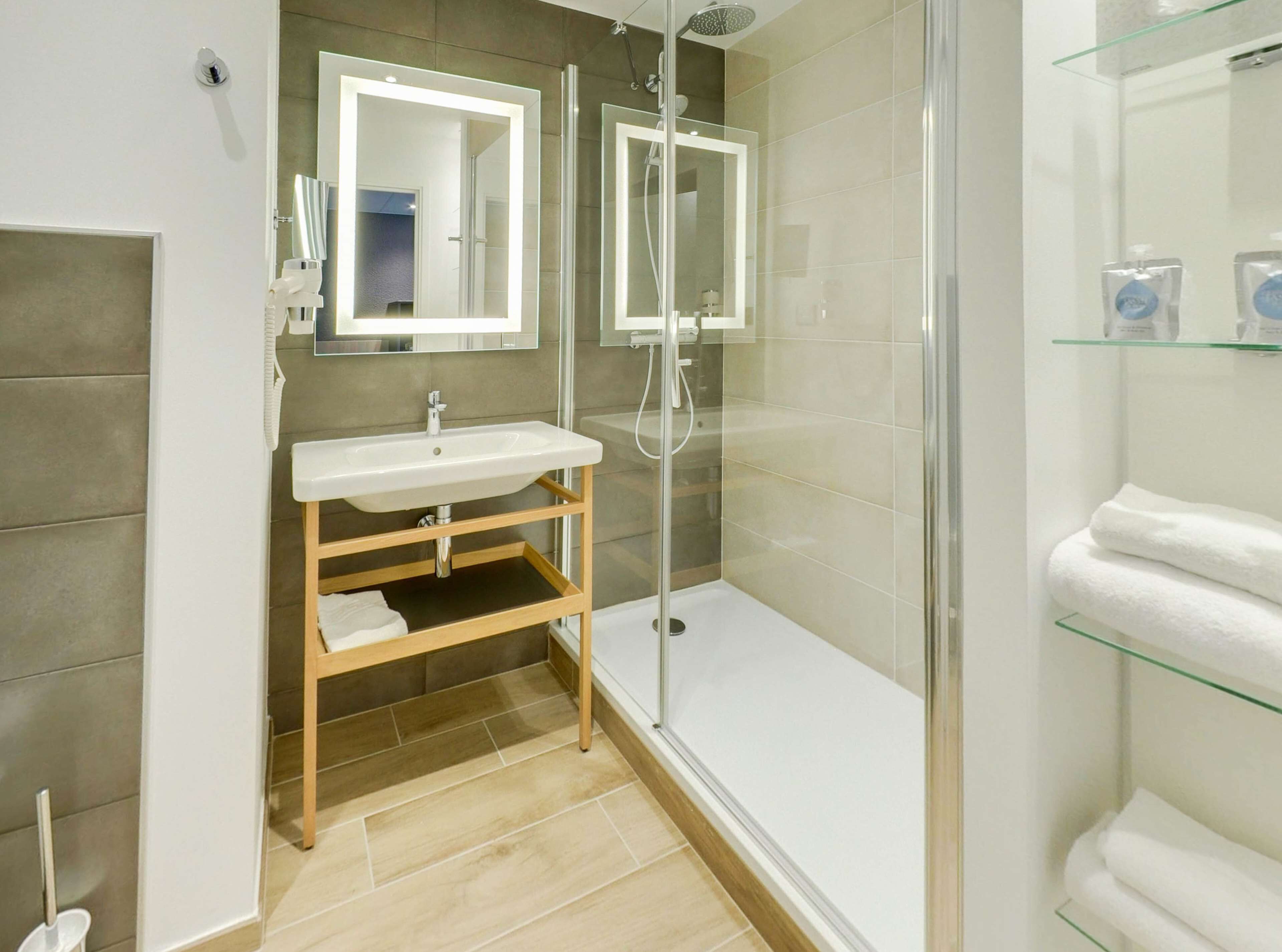 A modern bathroom with a glass-enclosed shower, a white sink, and a glass shelf with toiletries.