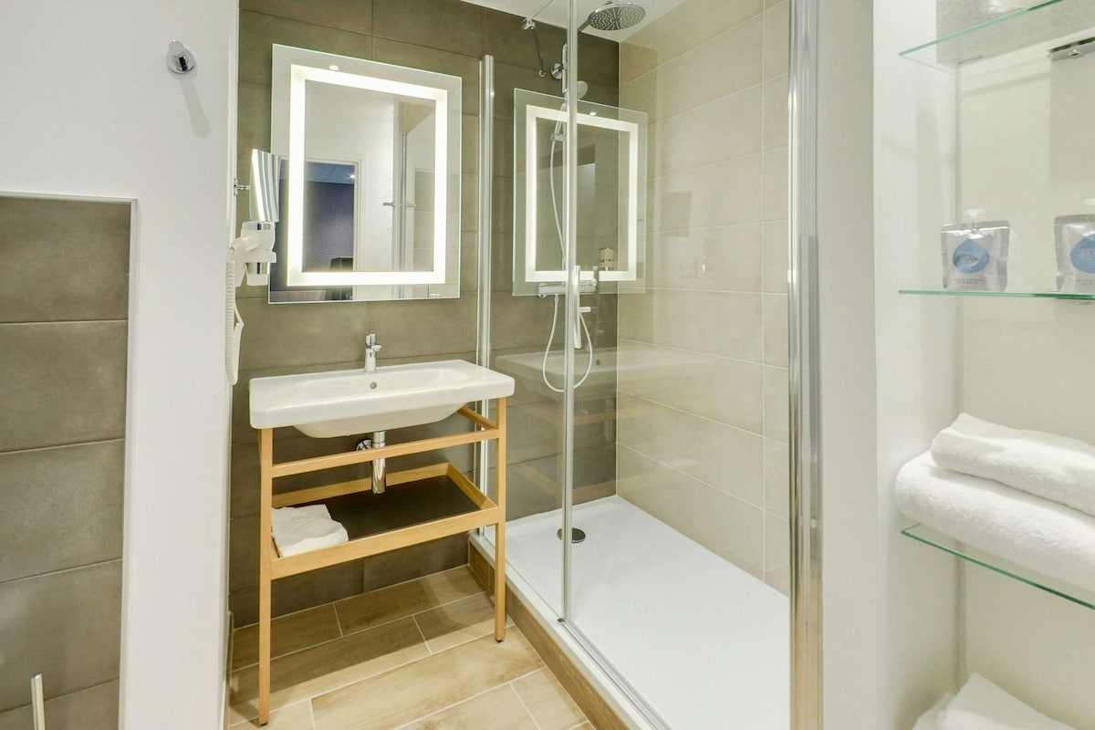A modern bathroom with a glass-enclosed shower, a white sink, and a glass shelf with toiletries.
