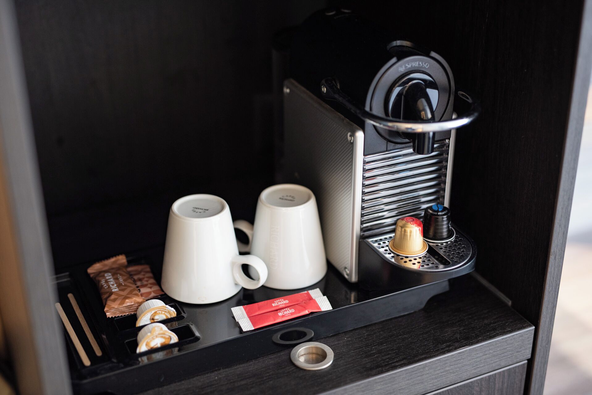 A coffee machine with two white cups and coffee pods on a black countertop.