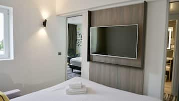 Habitación de hotel con cama, televisión de pantalla plana montada en la pared, ventana y puerta que da a otra habitación.