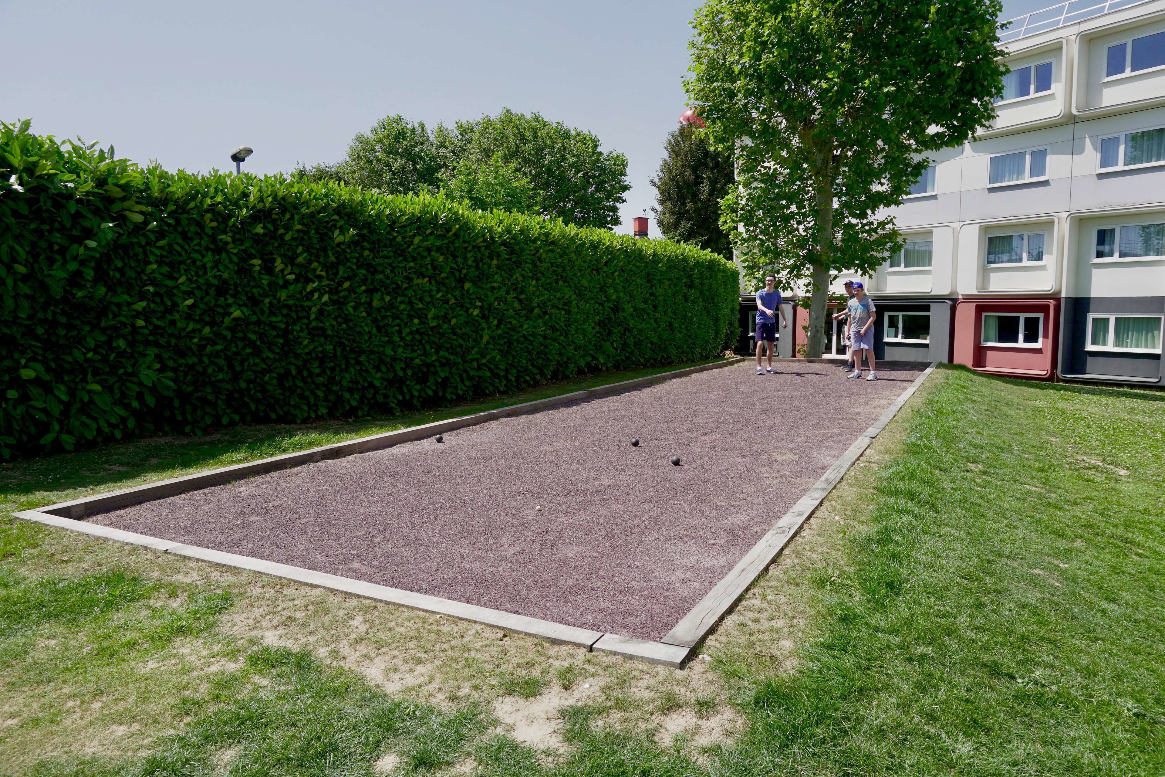 Un terrain de croquet avec une haie, de la pelouse et un bâtiment en arrière-plan.