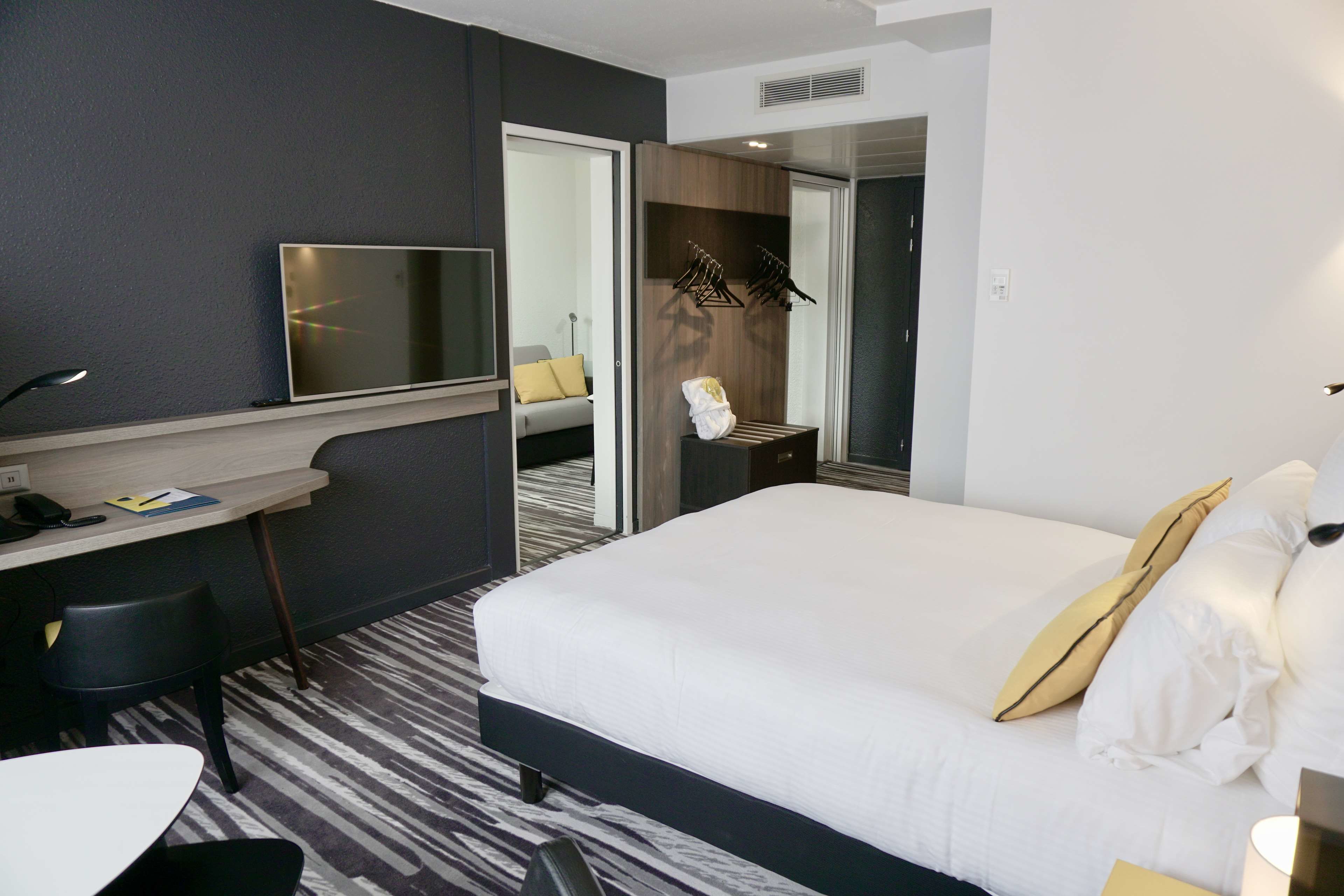 A hotel room with a bed, a desk, a chair, a TV, and a bathroom visible through an open door.
