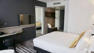 A hotel room with a bed, a desk, a chair, a TV, and a bathroom visible through an open door.