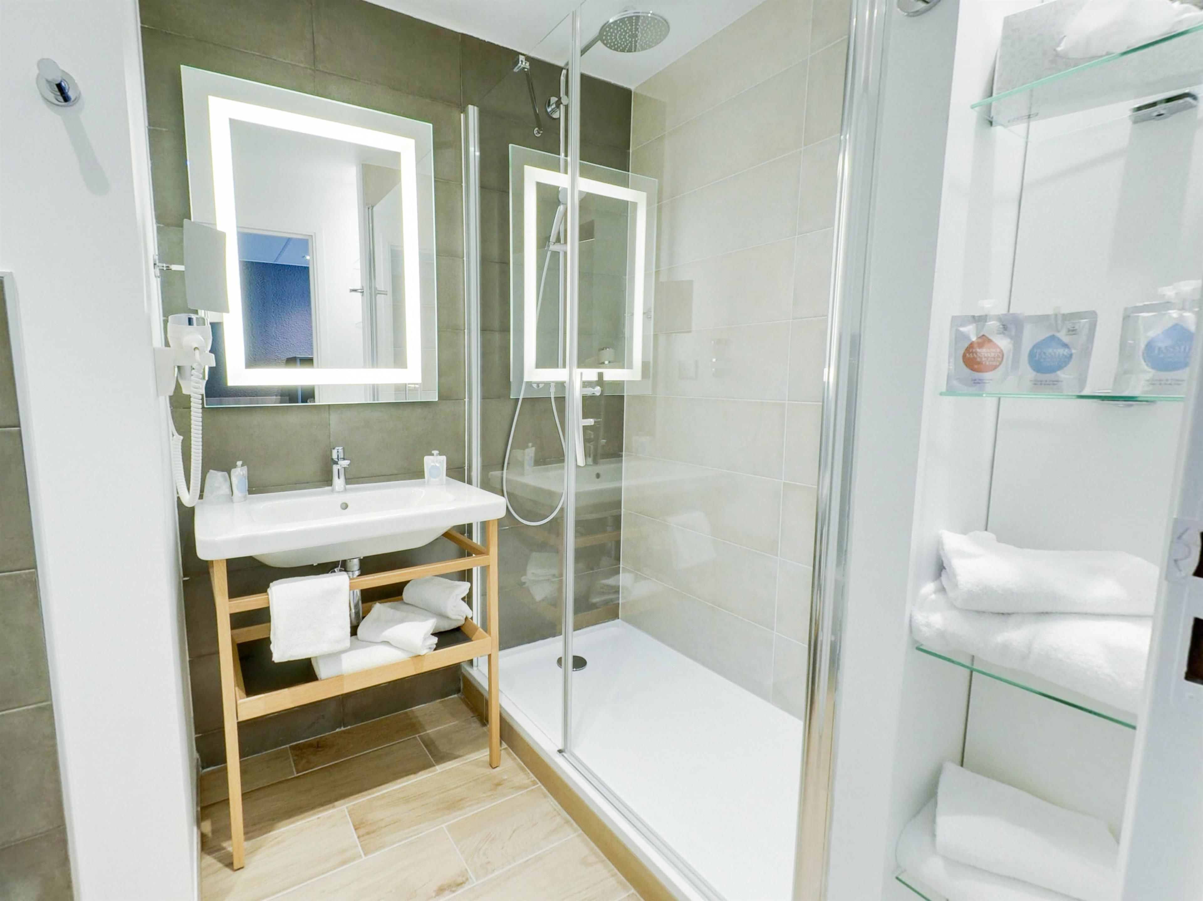 Un bagno moderno con cabina doccia in vetro, un mobile bagno in legno e uno scaffale in vetro con articoli da toilette.