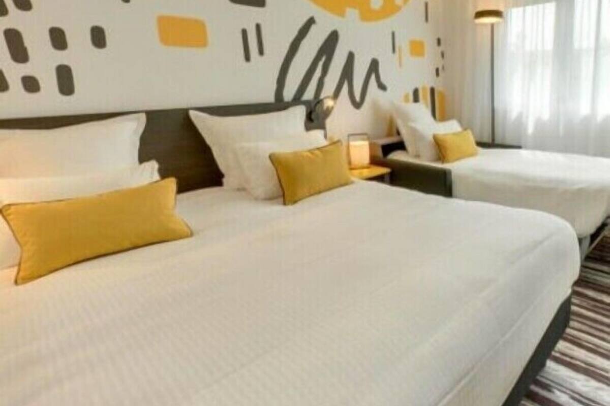 Une chambre d’hôtel avec deux lits, une grande fresque murale abstraite et une vue sur l’extérieur par la fenêtre.