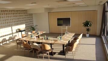 A conference room with a long table, chairs, a projector screen, and potted plants.