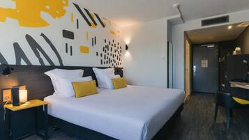 Ein Hotelzimmer mit einem großen Bett, einem Nachttisch mit Lampe, einer Wand mit abstrakter Kunst und einer Tür zu einem Badezimmer.