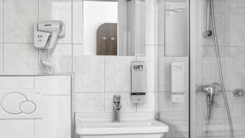 A modern bathroom with a glass-enclosed shower, a white sink, and a hairdryer mounted on the wall.