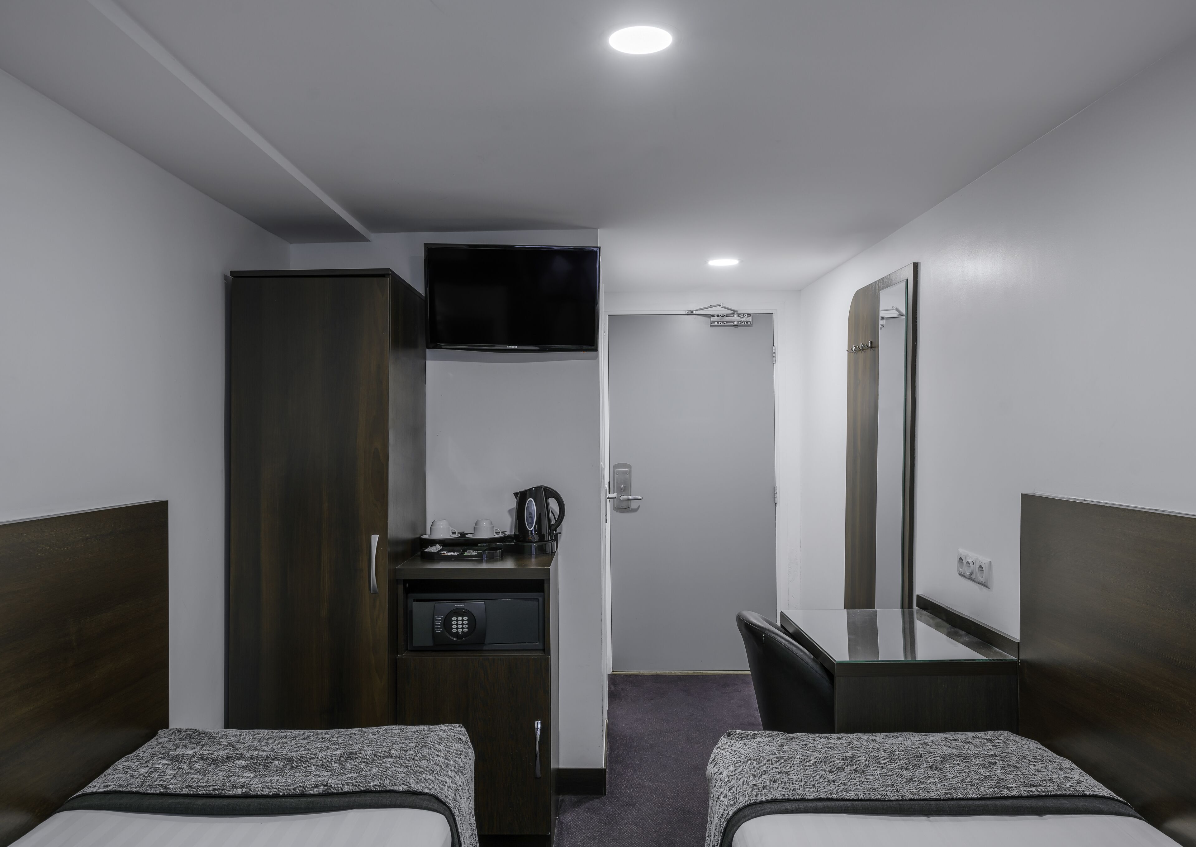 A hotel room with two beds, a desk, a wardrobe, a television, and a small kitchenette.