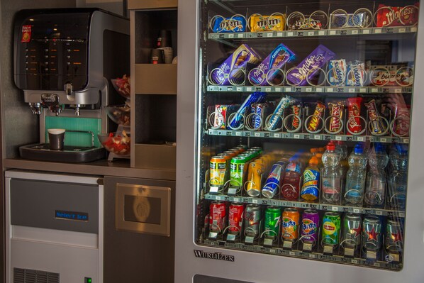 Un distributeur automatique proposant une variété de collations et de boissons, notamment une machine à café et un réfrigérateur portant l’inscription « Choisissez vos glaçons ».