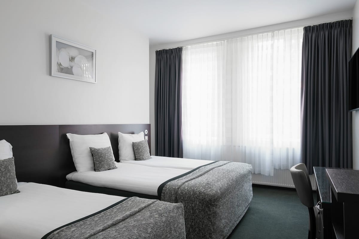 Ein Hotelzimmer mit zwei Betten, einem Schreibtisch und einem großen Fenster mit Vorhängen.