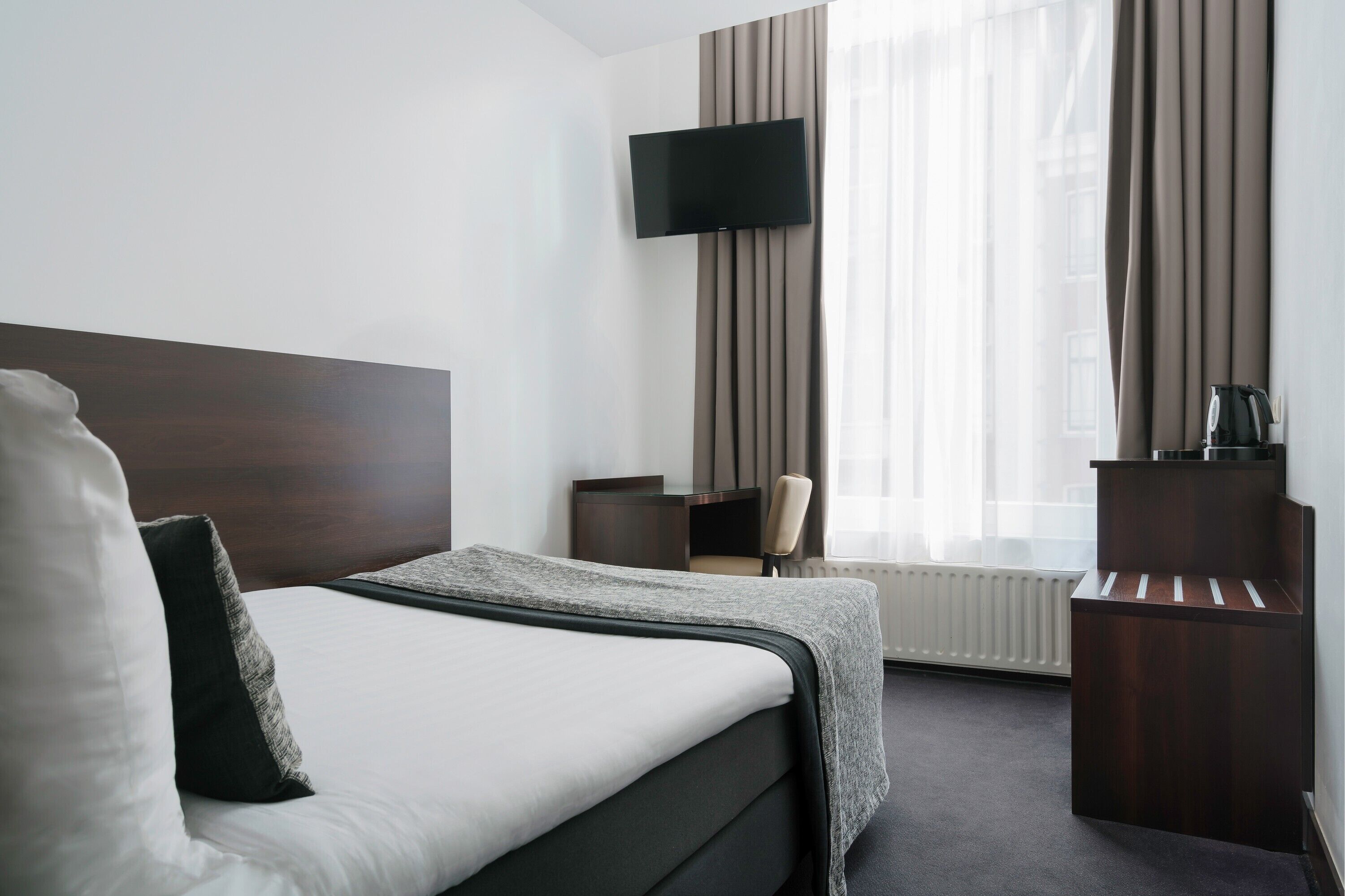 Una habitación de hotel con cama, escritorio, silla, televisor y radiador.