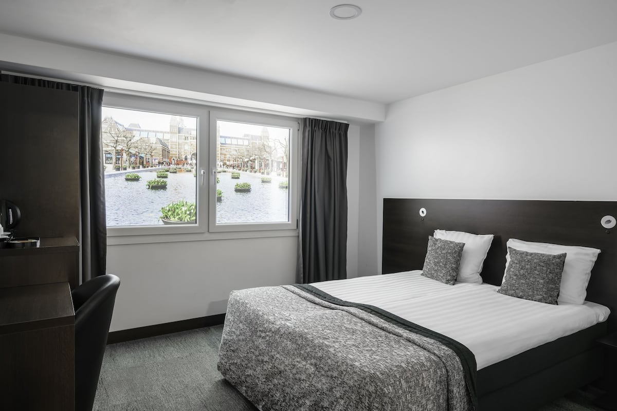 Ein Hotelzimmer mit Bett, Schreibtisch und Fenster mit Blick auf einen Kanal und Gebäude.