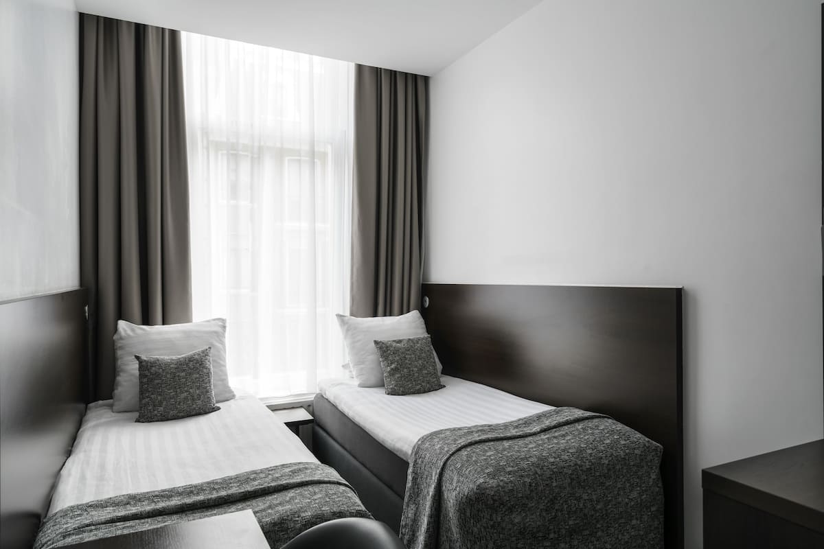 Ein modernes Hotelzimmer mit zwei Einzelbetten, einem großen Fenster mit transparenten Vorhängen und einem dunklen Kopfteil.